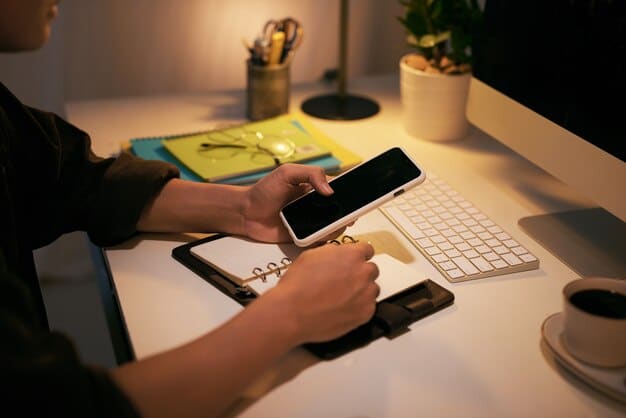 A person's hands typing on a laptop keyboard, with a smartphone beside it showing a security verification code from a finance app. The background is a cozy home office with bookshelf and lamp.