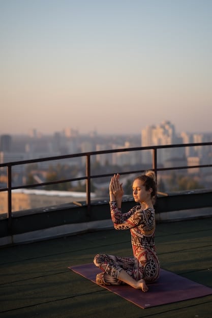 A woman is doing yoga poses at sunrise on a rooftop in Mexico City. The city skyline is visible in the background, with the rising sun casting a warm glow over the scene. The woman is wearing yoga attire and appears focused and serene.
