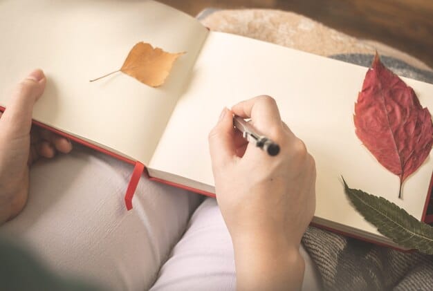 A close-up shot of a hand holding a pen and writing in a journal. The background is slightly blurred, showing a cozy room with a lamp and books. The image focuses on the act of writing as a personal and introspective activity.