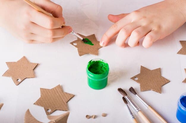 Close-up of hands crafting a star-shaped Christmas ornament using recycled cardboard and colorful paint. The focus is on the detail of the ornament and the act of creating something beautiful from simple materials.