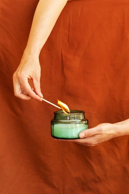 Hands delicately pouring soy wax mixed with orange essential oil into a glass candle container, with a wooden stick holding the wick centered.