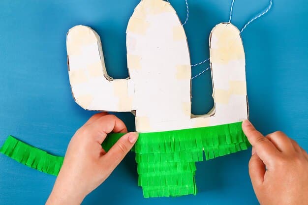 A close-up of hands assembling a star-shaped piñata frame from cardboard. The pieces are being glued together, showing the initial stages of creating the structure.