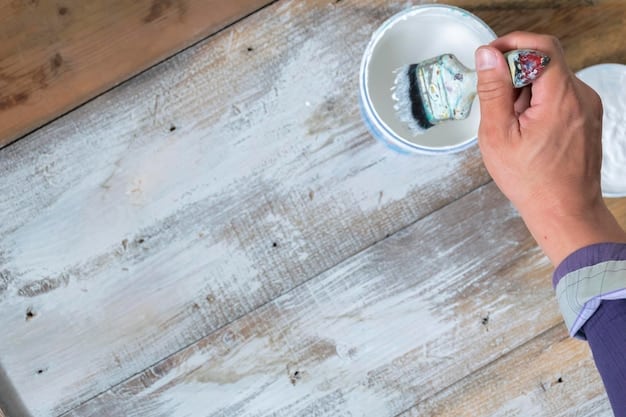 A close-up of a person's hands applying chalk paint to a wooden dresser with a brush. The dresser is partially painted, showcasing the color difference and the texture of the chalk paint. There are paint cans and tools nearby, indicating a DIY project in progress.