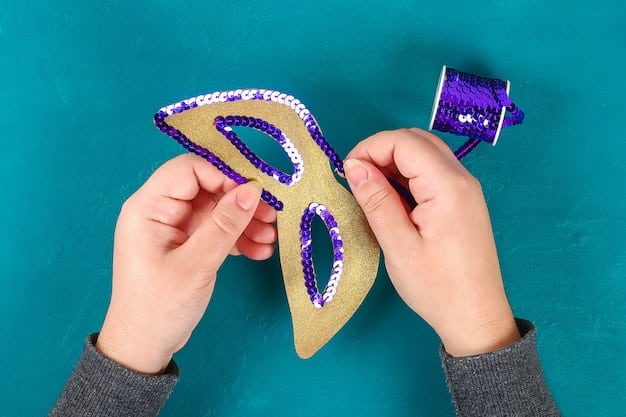 A person's hands carefully sewing sequins onto a colorful felt lucha libre mask. The background is blurred but shows more mask-making materials and tools.