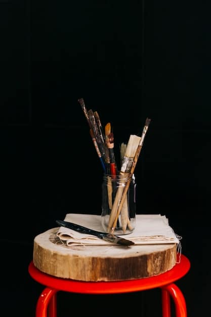 A close-up shot of various tools and materials used in papier-mâché art. The composition includes shredded newspaper, a container of glue, brushes, vibrant acrylic paints in small pots, scissors, and a pair of pliers. The arrangement is artistic and visually engaging, highlighting the diversity of textures and colors involved in the craft.