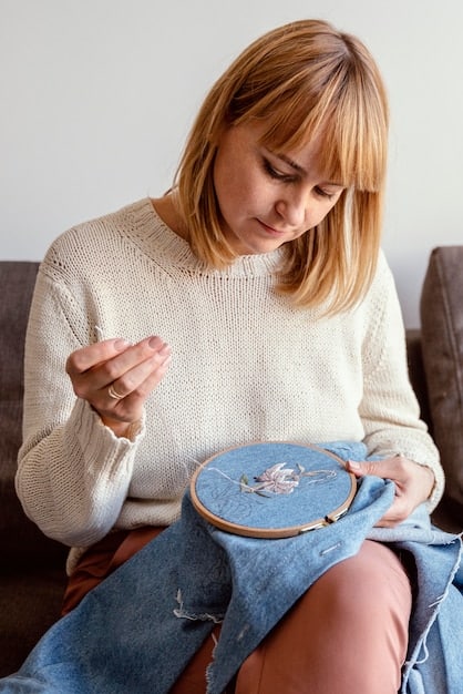 A person using a punch needle to create embroidery on a piece of cloth stretched in an embroidery hoop. The focus is on the needle and the colorful yarn being punched through the fabric, highlighting the details of the technique.