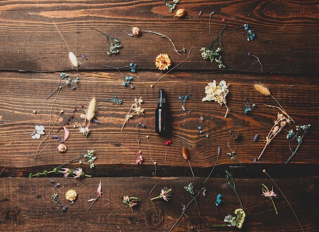 An overhead shot of various dried flowers and pressed leaves laid out on a wooden table, with tools and materials for crafting flower frames scattered around. The scene showcases a creative workspace.