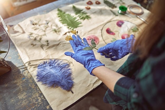 A crafter's hands carefully arranging pressed flowers and leaves on a piece of decorative paper, preparing to glue them down to create a framed artwork. The focus is on the delicate placement of the natural elements.