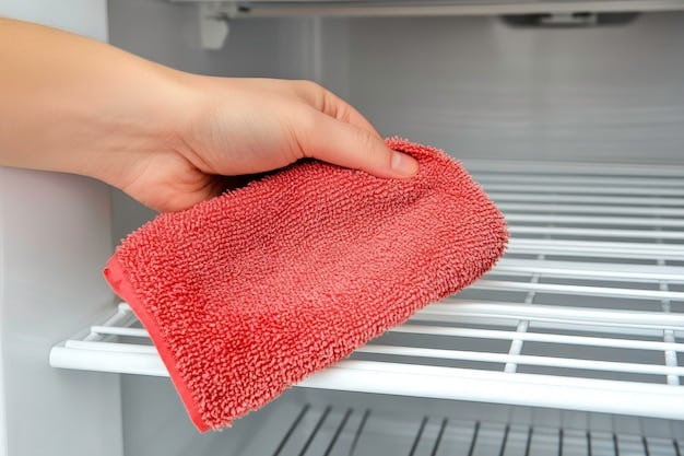 Close-up of hands wiping down a refrigerator shelf with a cleaning cloth, emphasizing the importance of hygiene in food storage.