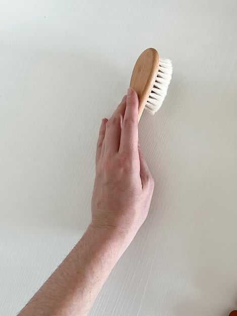 A person's hands gently scrubbing a stained white t-shirt with a soft bristle brush, applying a paste made from baking soda, lemon juice, and vinegar. The focus is on the scrubbing motion and the application of the paste on the stain.