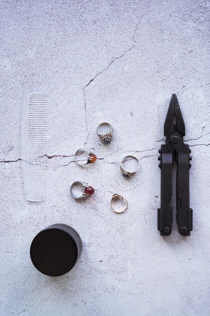 An overhead shot of various tarnished silver jewelry pieces like rings, necklaces, and earrings scattered on a dark, reflective surface, showcasing the oxidation and dullness before cleaning.