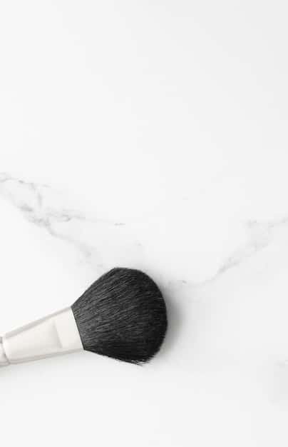 A person laying out makeup brushes to dry on a clean white towel. The brushes are spaced out evenly, in a clean, well-lit area. The photo focuses on the brushes that are aligned horizontally.