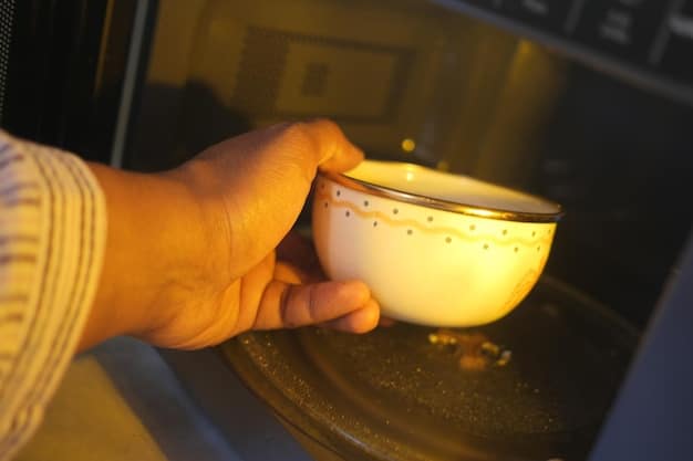 An angled close-up showing a person carefully placing a microwave-safe bowl filled with a clear liquid and lemon slices inside a microwave. The inside of the microwave is clean and well-lit, suggesting a focus on preparation for cleaning. The bowl is centered, and the person's arm is partially visible, reinforcing the action of placing the cleaning solution.